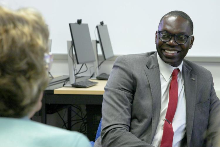 Lt. Governor Garlin Glichrist II sits, smiling in front of two computer monitors.