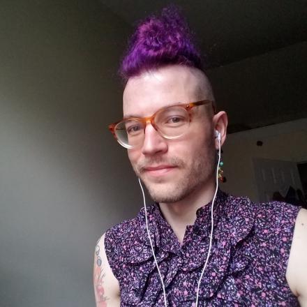 Photograph of Ximón, in a sleeveless ruffled floral shirt and purple hair pulled into a bun.