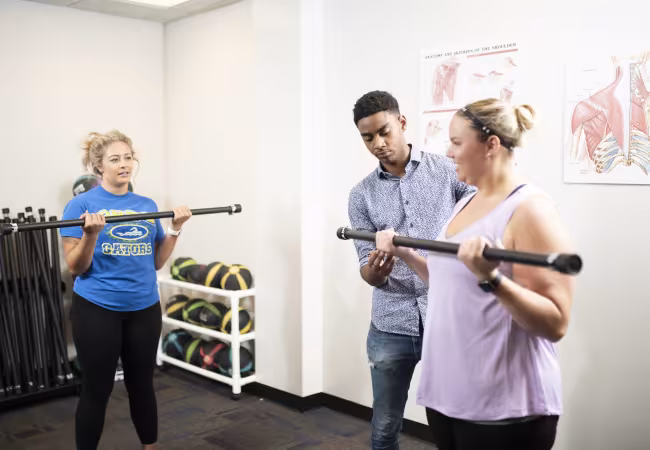 In a gym, person helps another use a weight bar
