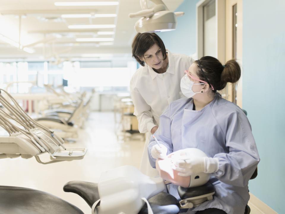 Dental student cleaning teeth and professor giving guidance