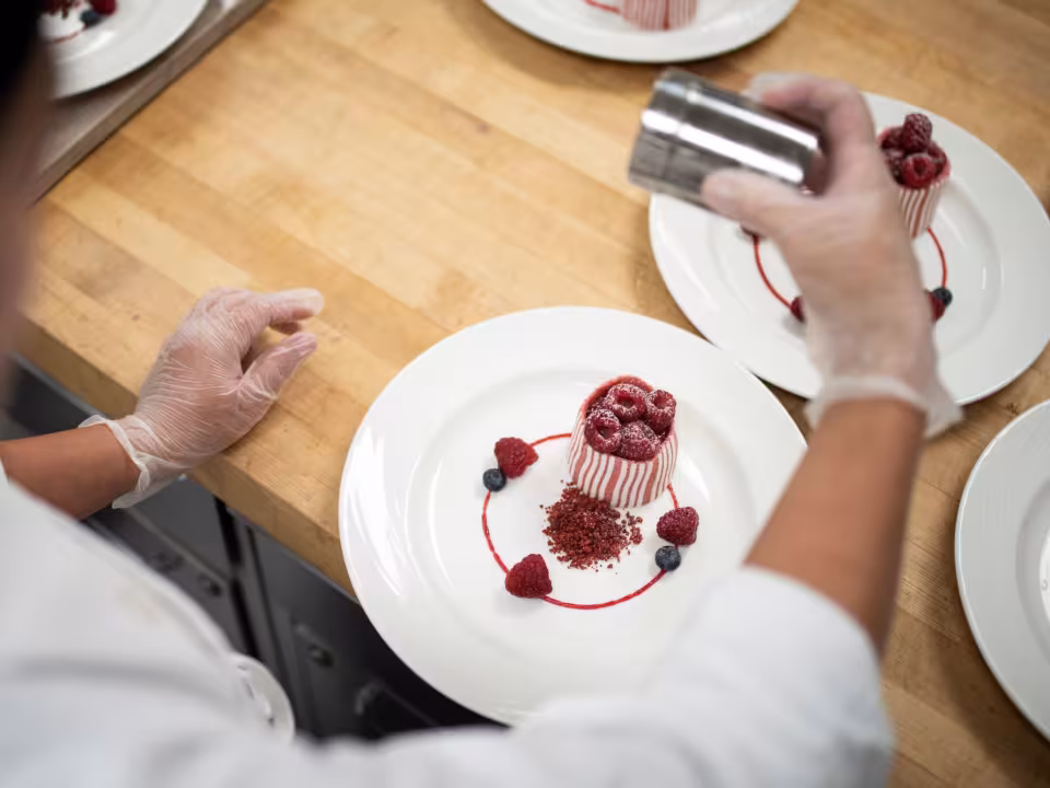 Student sugars a baked good in a culinary lab.