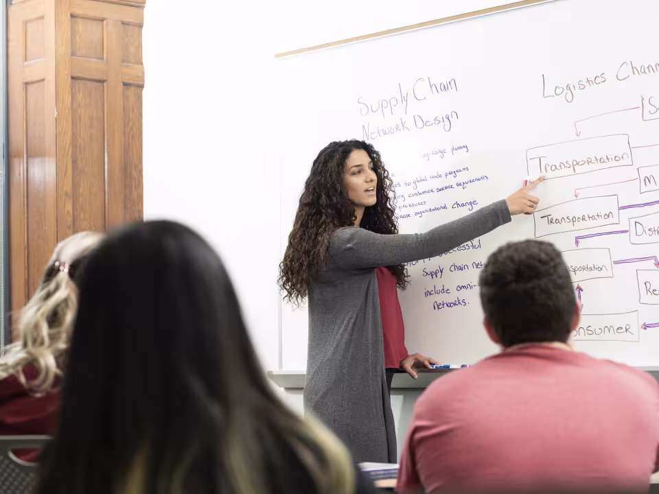 Student presents her work on the whiteboard in a Supply Chain Operations course.