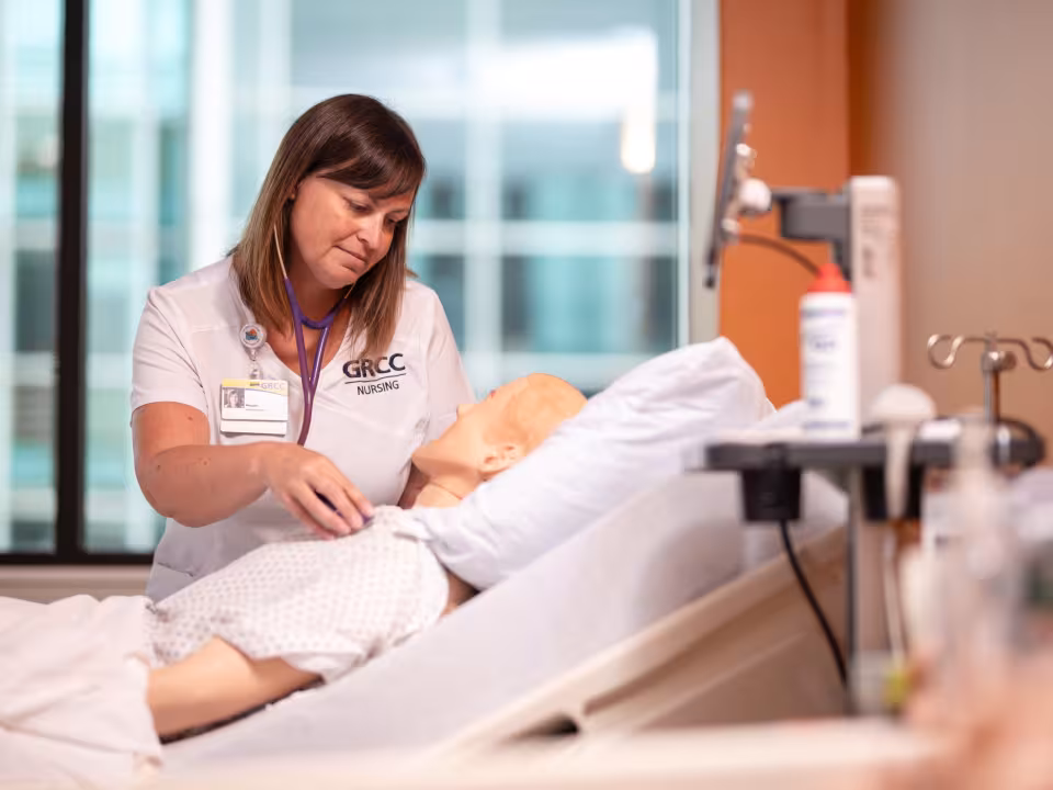 A GRCC nursing student works with a mannequin on a hospital bed.