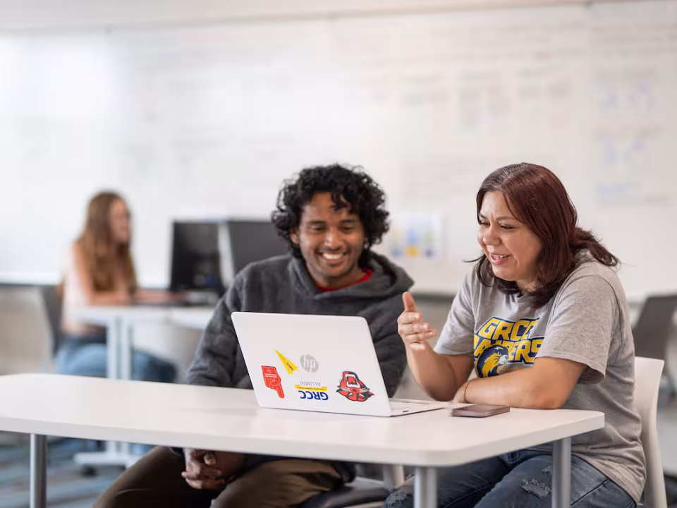 Two students work together on a laptop in a classroom.
