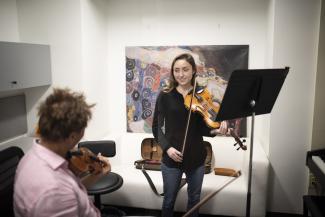 Student holding a violin in a practice room.