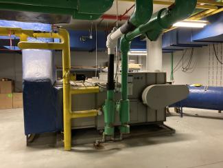 A large, floor-mounted machine connects to yellow and green pipes. 