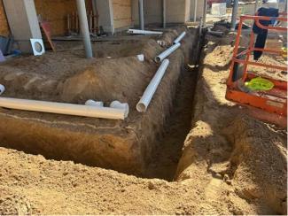 An outdoor sanitary sewer trench and disconnected white piping.