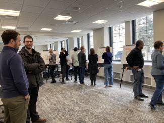 Several people examine boards on easels in a large room.