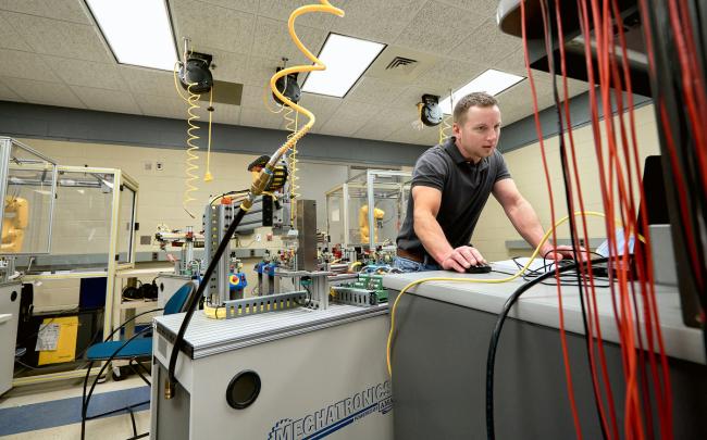 A male student works on the mechatronics line surrounded by equiprment at GRCC.