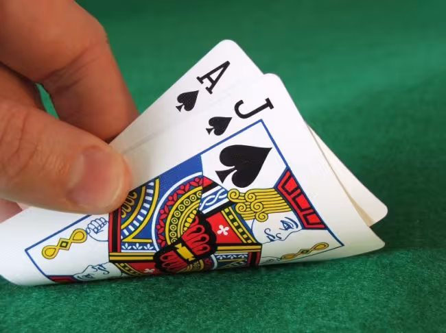 A hand is turning over two cards: the ace and jack of Spades.