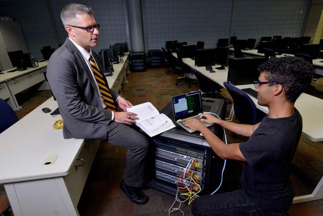 Professor Drew Rozema speaking with a student in a computer lab.
