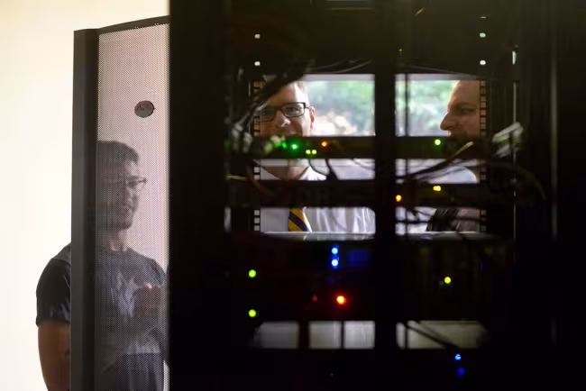 GRCC students and professor looking at a computer server, viewed from the back.