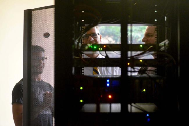 GRCC students and professor looking at a computer server, viewed from the back.