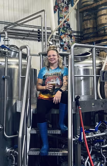 GRCC Alumnus Casey Brunetti poses near brewing equipment with a glass of beer in hand.