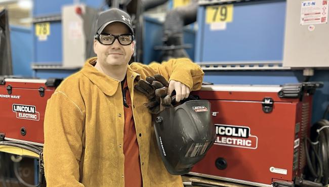 Cory Stout posing with his welding gear in the lab. 