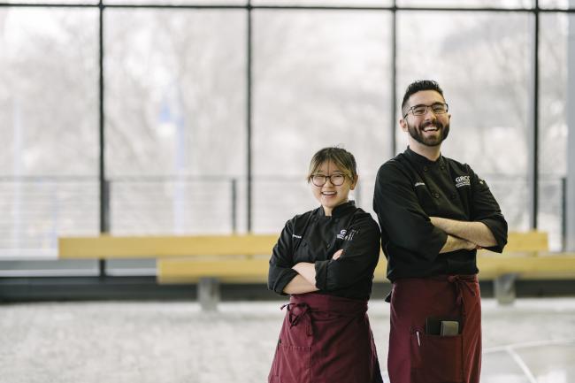 Two student chefs stand with arms crossed