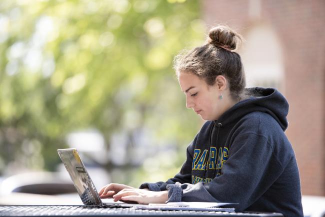 A GRCC student working outdoors on a laptop.