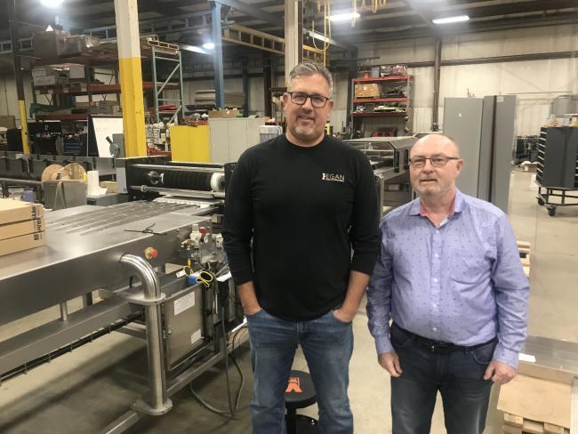 Mike Sherd and Bob Cisler stand near a machine they created to make candy.