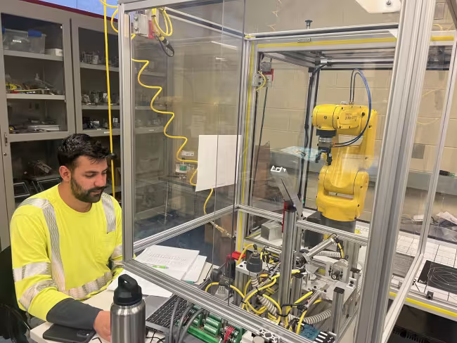 A person sits at a computer near a robotic arm.