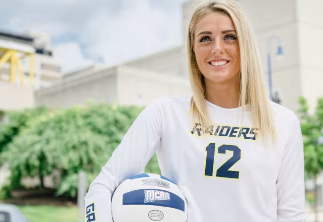 Portrait of Annie Holesinger in uniform holding a volleyball.