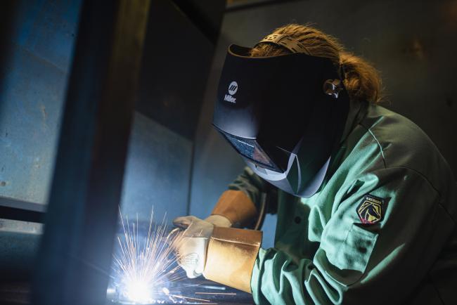 Welding student working, creating sparks while wearing protective gear.