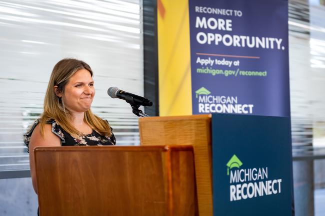GRCC student Morgan Brink standing at a podium and speaking about the Michigan Reconnect scholarship.