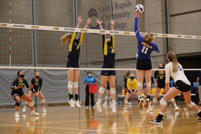 Action shot of GRCC volleyball players leaping to block a spike.