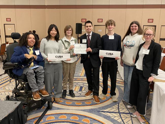 Seven students pose, some holding an award and paper signs reading "Cuba."