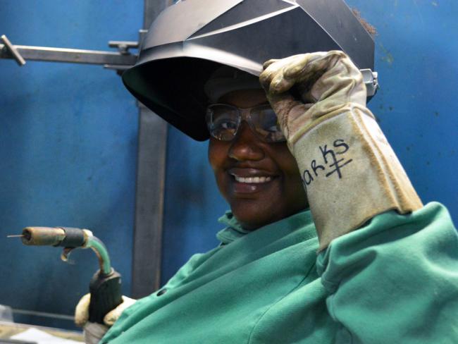Welding student and Metallica Scholar Uniqua Sparks smiles as she lifts up her welding helmet.