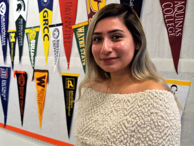 UPrep student Karla Lopez standing in front of college pennants.