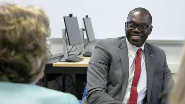 Lt. Governor Garlin Glichrist II sits, smiling in front of two computer monitors.
