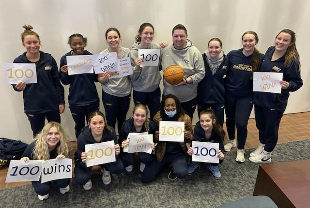 The women's basketball team with coach Glazier, holding up 100 win signs.