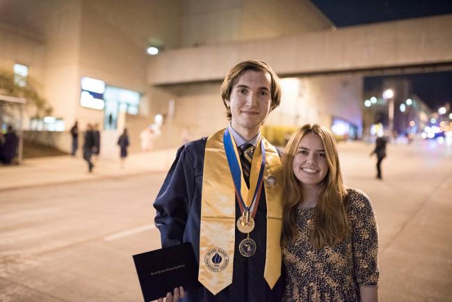 Marcus Barissi, in a graduation cap and gown, stands with a young woman on Lyon Street.