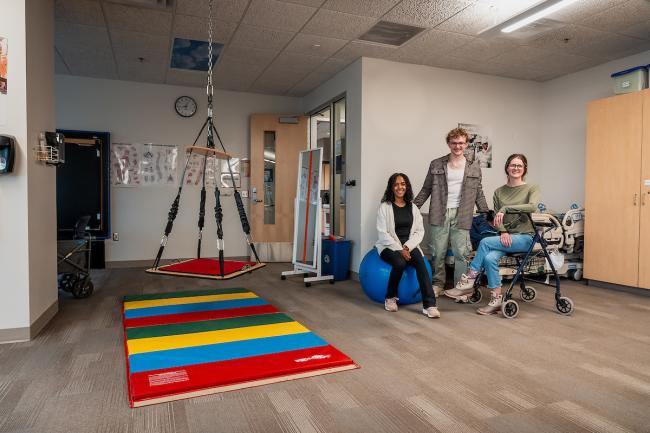 Students pose in the Occupational Therapy Assistant lab surrounded by various pieces of equipment.