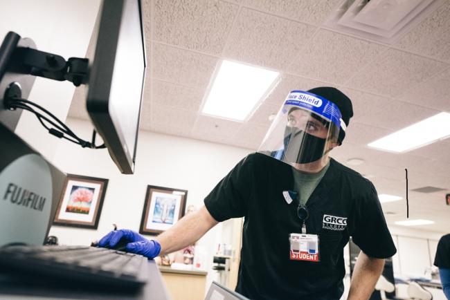 Radiology student with face coverings looking at xrays on a computer screen.