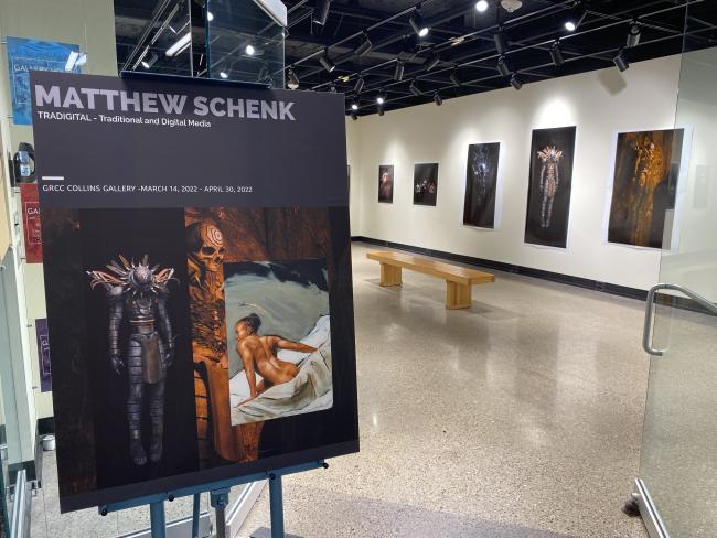 A sign for the exhibit with artwork in the background.