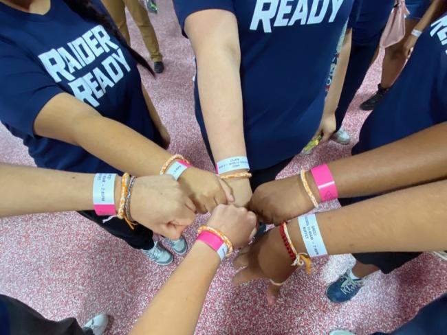People wearing Raider Ready t-shirts do a group fist bump.