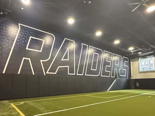 An indoor turf field with the word "Raiders" on the wall