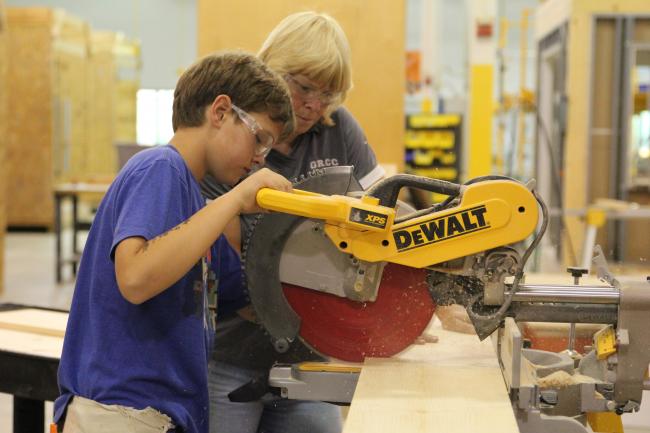 Camp student working with a saw supervised by a GRCC staff member.