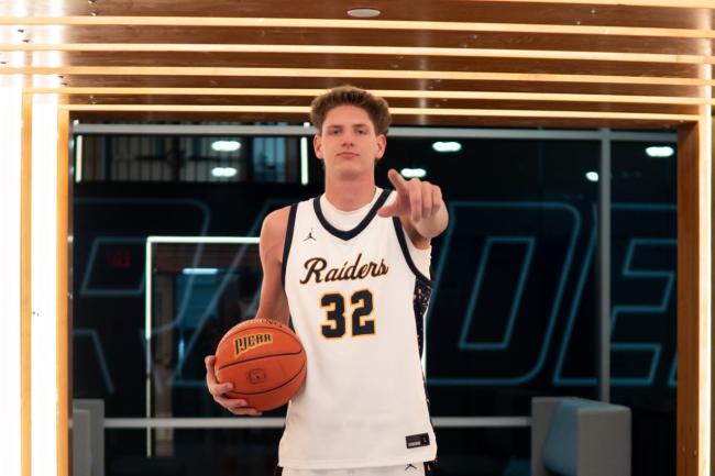 GRCC athlete Jakob Chapman stands confidently holding a basketball and pointing at the camera