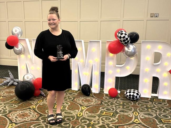 Kailee Potgeter poses with an award in front of balloons and large letters spelling NCMPR.