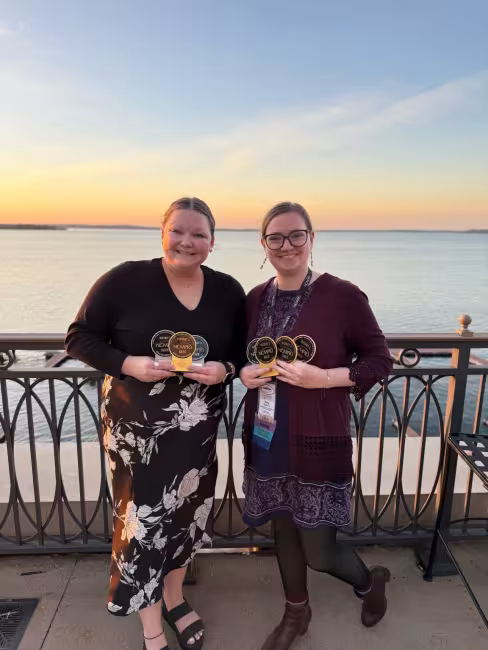 Two members of the marketing team pose holding seven awards.