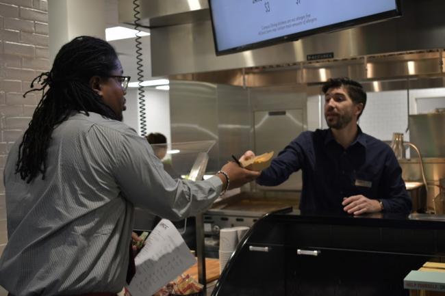 Campus Dining Director Keaton Krupa reaches over the counter to serve food to a GRCC student.