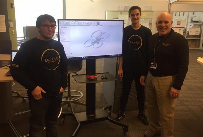 GRCC instructor Art Ward poses with Launch U students Conner Koop and Evan Oeverman standing in front of a monitor showing a photo of a drone.