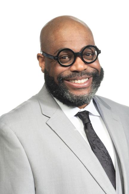 Maurice Baker in a gray suit and glasses.