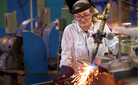 A female welding student working on a project, creating sparks