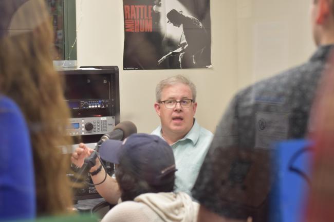 Len O'Kelly sitting in a broadcast booth surrounded by students.