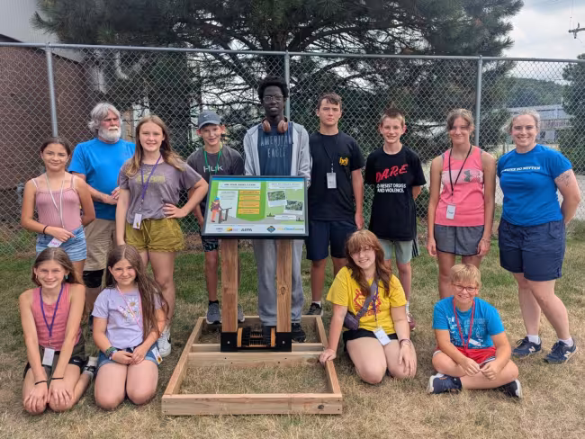 11 campers and instructors pose with a boot brush station and plaque.