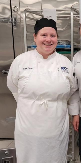 Quinn Thomas in a white chef coat and apron.