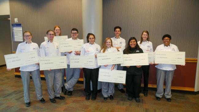 Culinary students hold up giant checks from Experience Grand Rapids.